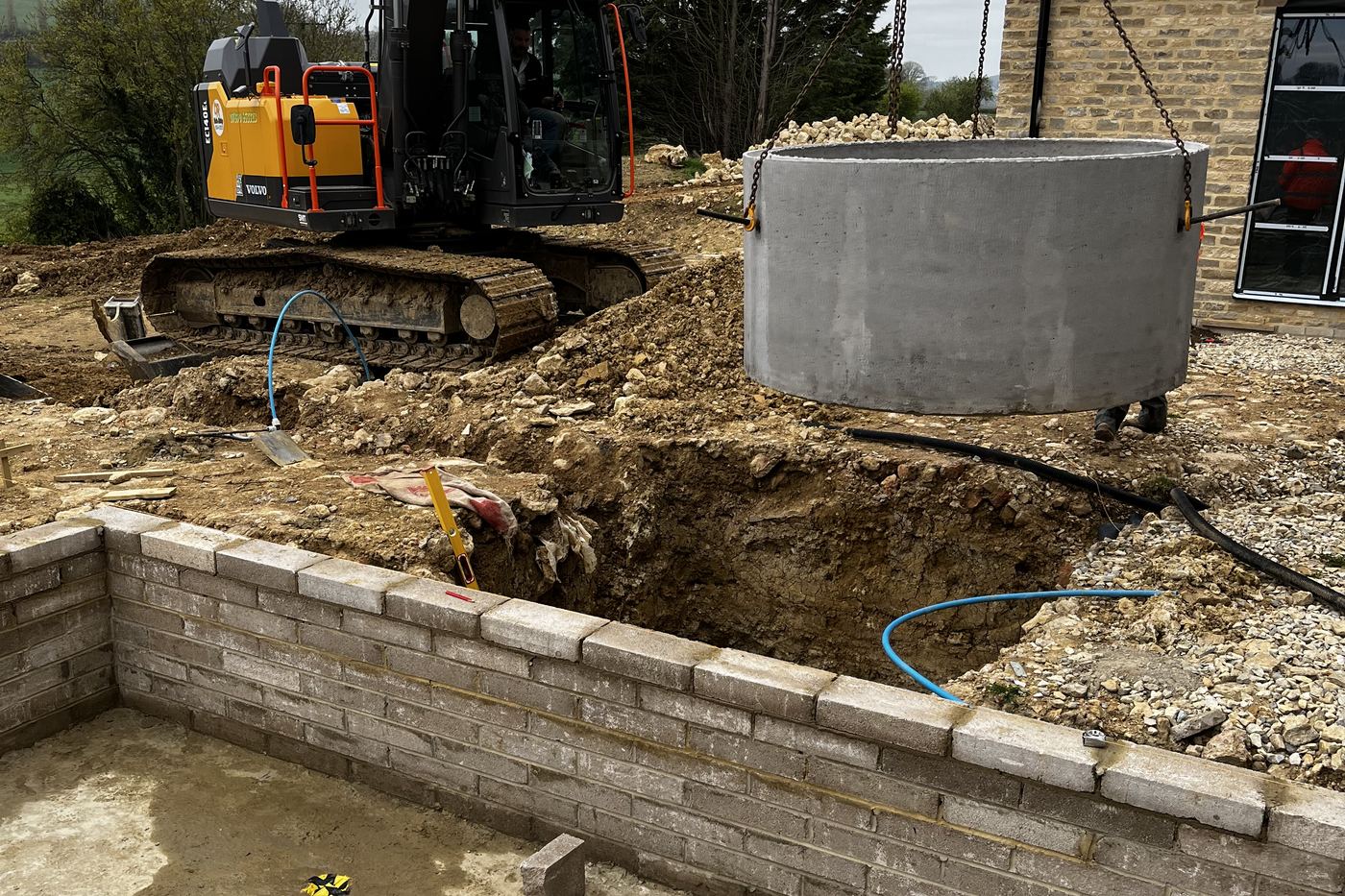 Excavator setting a concrete treatment tank into an excavation near Andover